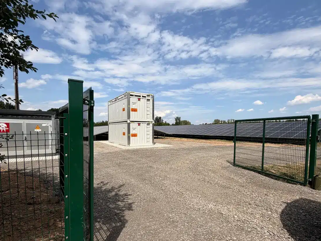 Zufahrt zum Co-Location-Standort mit gestapelten Batteriespeicher-Containern und Solarpark