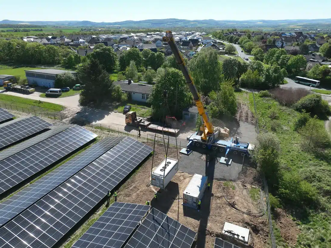 Luftaufnahme: Kran setzt Batteriespeicher-Container in einen bestehenden Solarpark